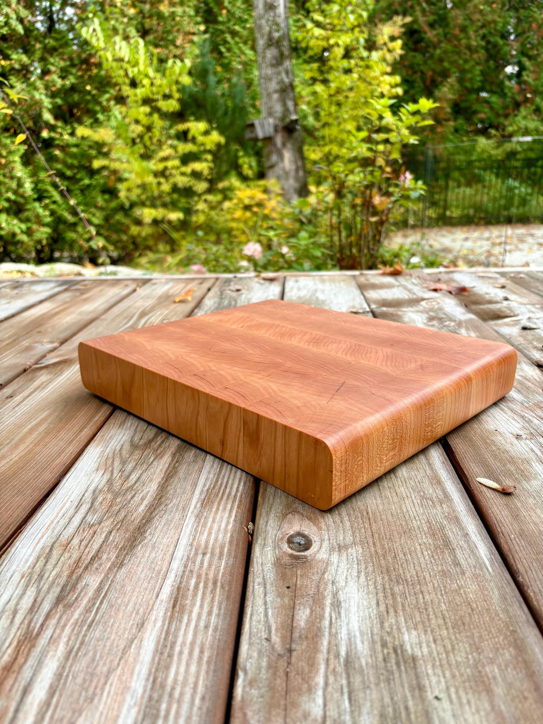 Planche à découper en cerisier, bois debout, 12,75 x 10,5 po, sur une terrasse en bois à l’extérieur, vue en angle