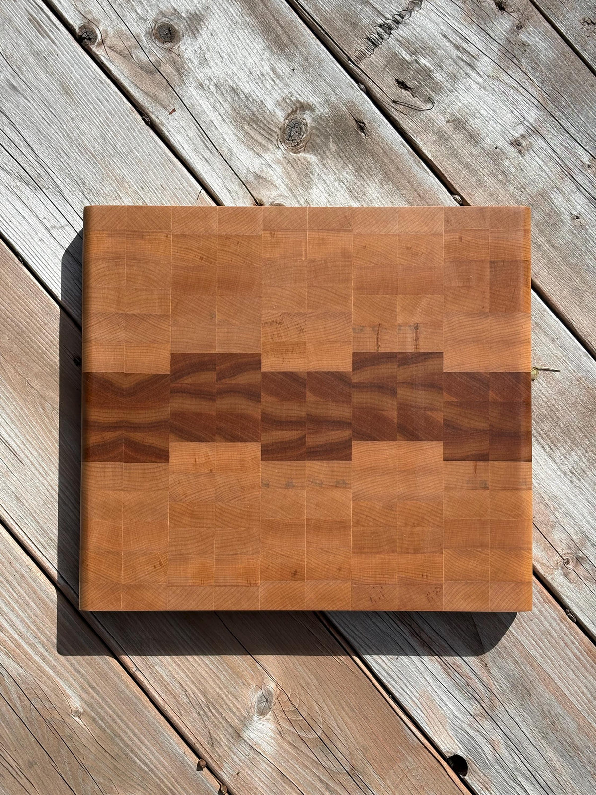 Cherry and maple end grain cutting board 13 x 11.75 in on a wood deck, top view
