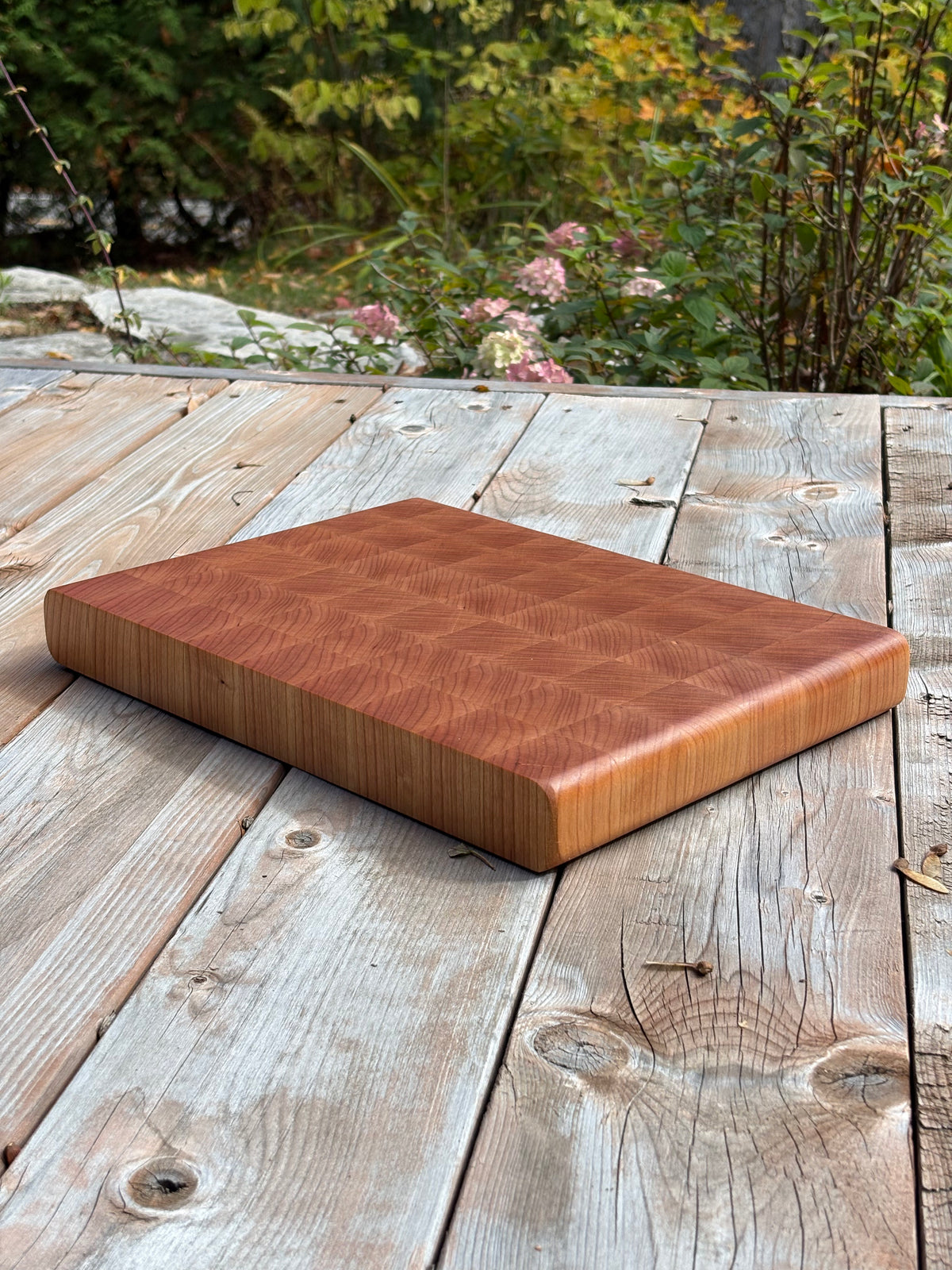 Cherry end grain cutting board 14.5 x 10.5 in on a weathered wood deck, angled view