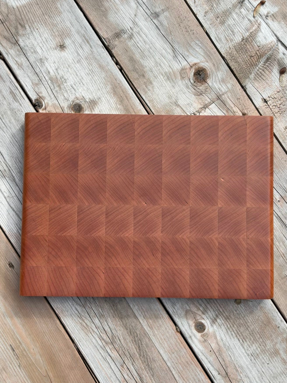 Cherry end grain cutting board 14.5 x 10.5 in on a weathered wood deck, top view