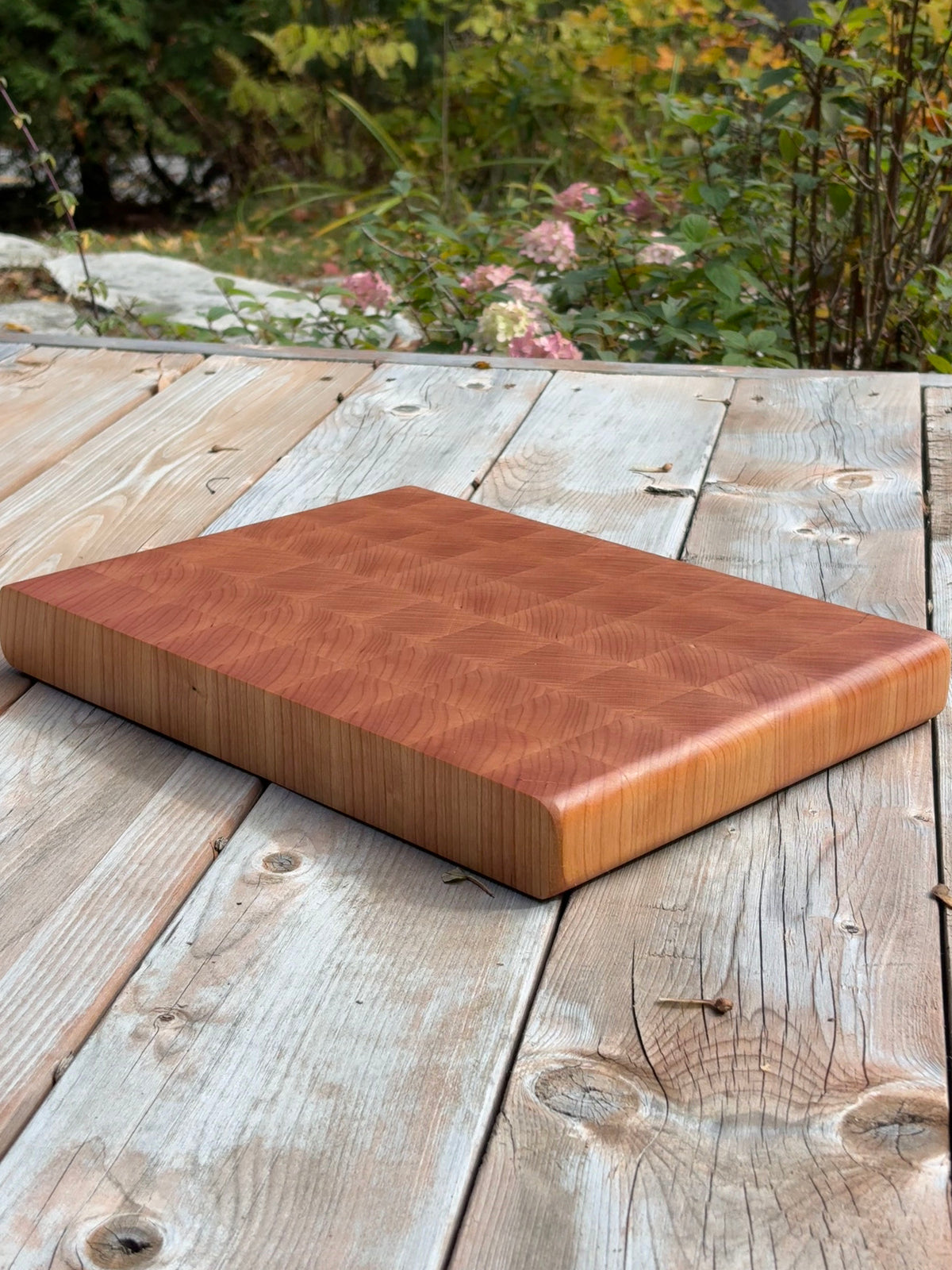 Cherry end grain cutting board 14.5 x 10.5 in on a wood deck outdoors, angled view