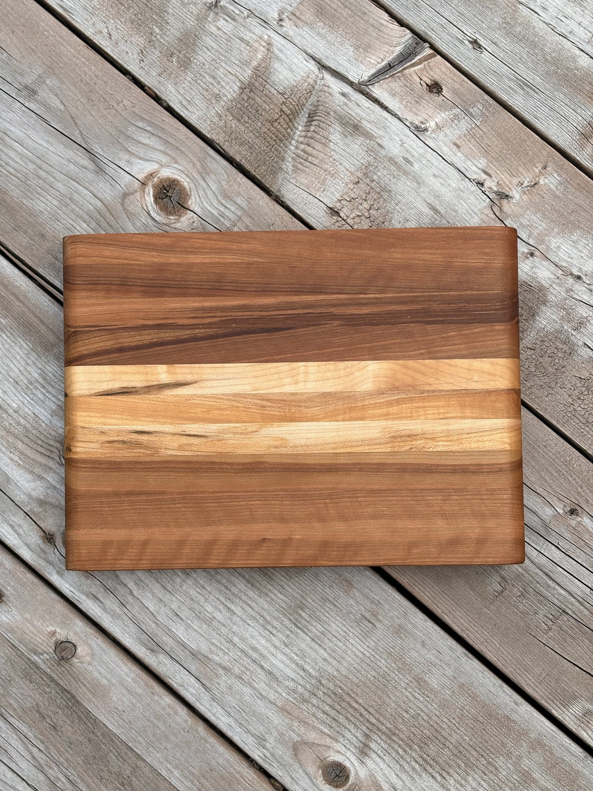 Petite planche à découper cerisier et érable de 11,25 x 8,25 po (vendue) avec bande centrale pâle, vue de dessus sur une terrasse en bois