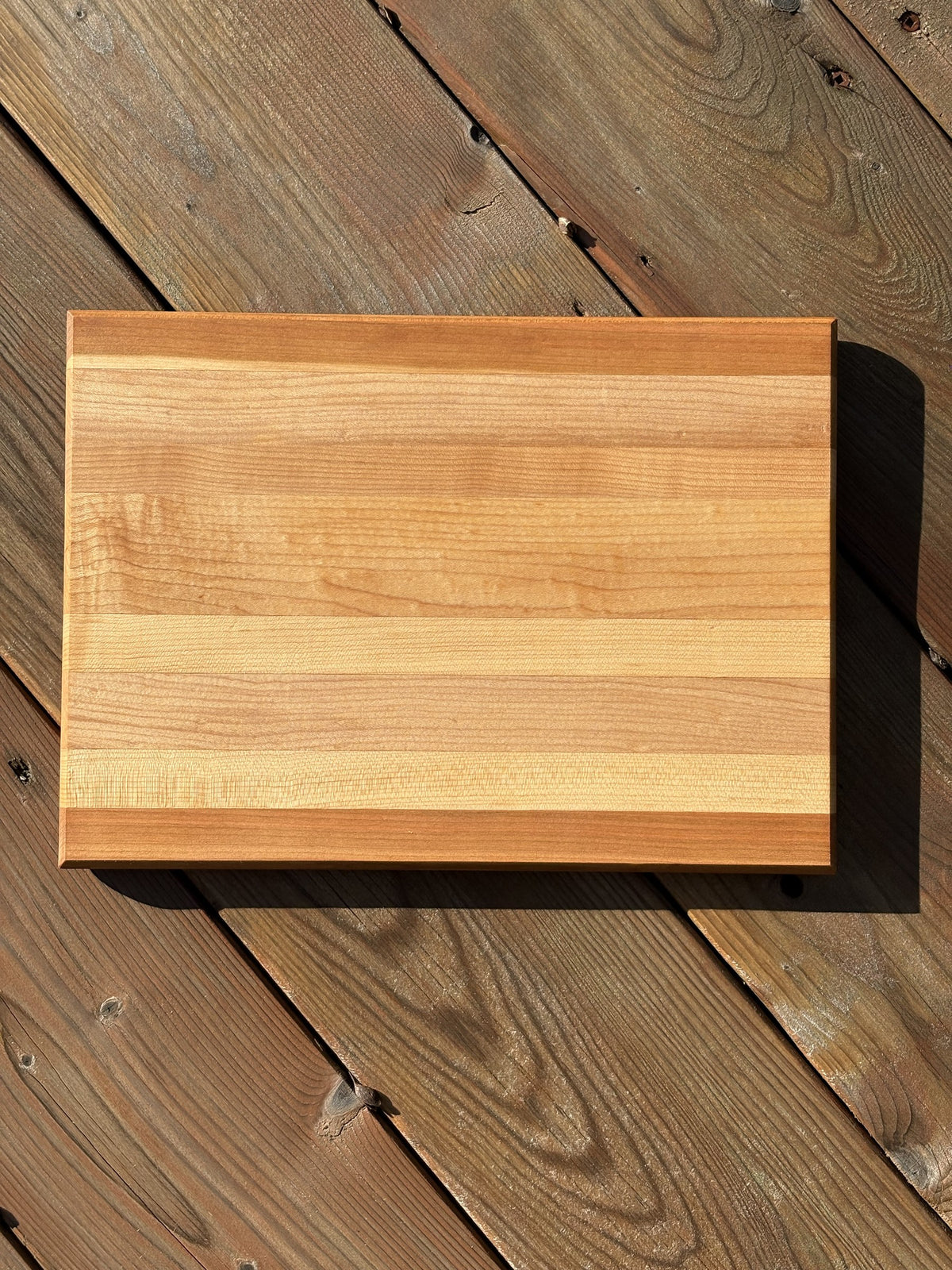 Planche à découper rayée cerisier et érable (vendue), vue de dessus sur une terrasse en bois