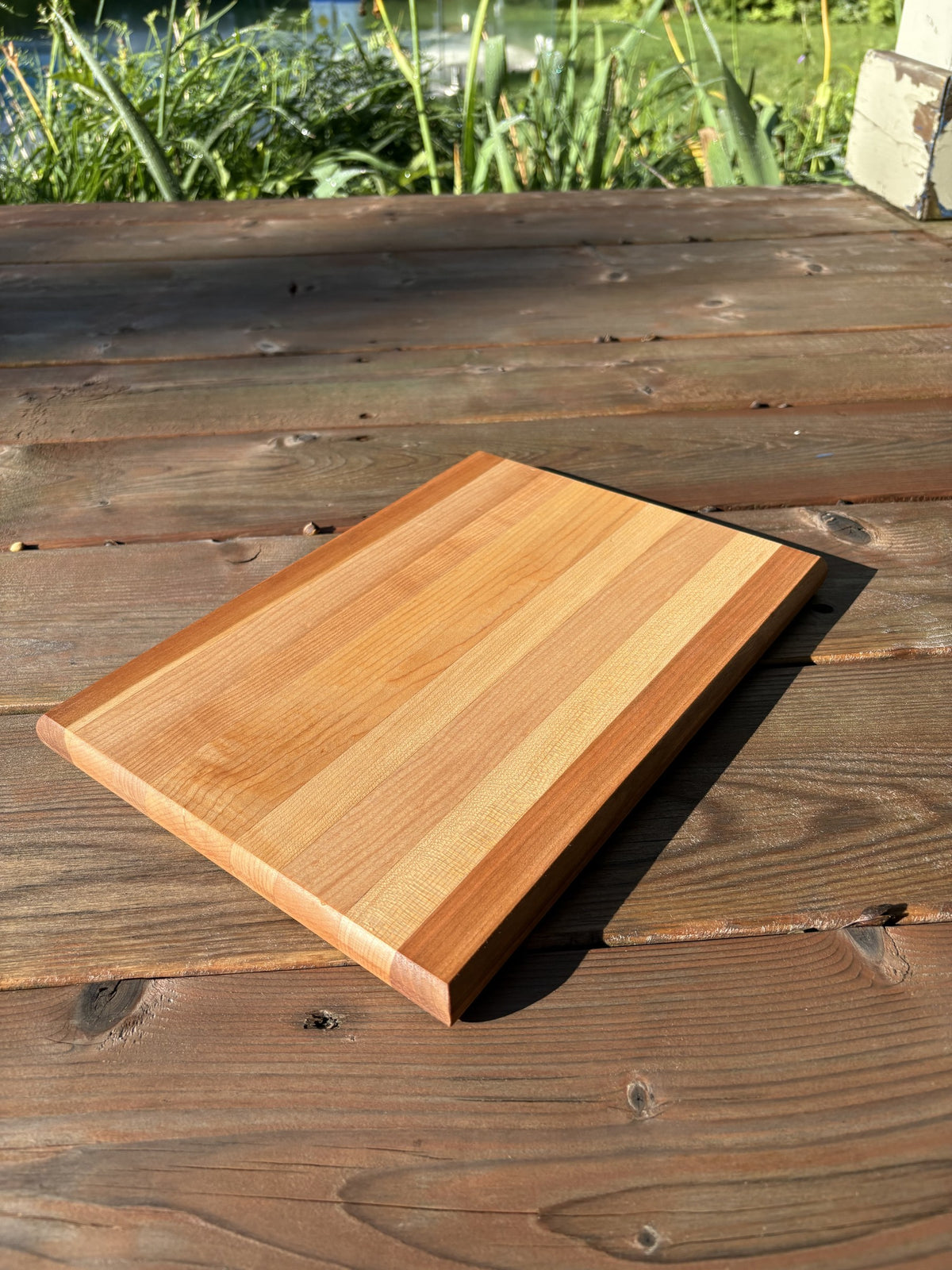 Planche à découper rayée cerisier et érable (vendue), vue en angle sur une terrasse en bois, plantes en arrière-plan