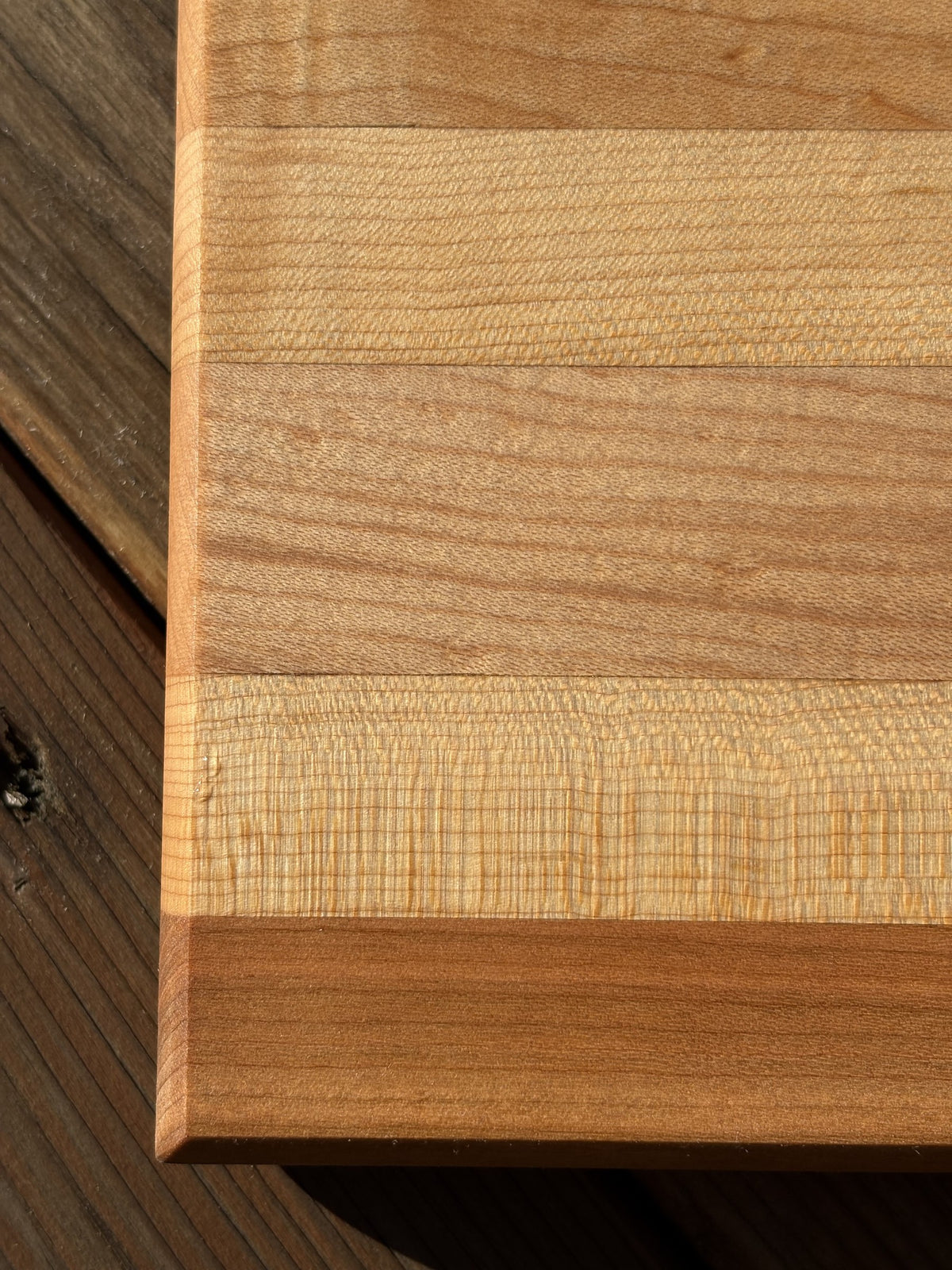 Gros plan sur un coin de la planche à découper rayée cerisier et érable, montrant le grain du bois